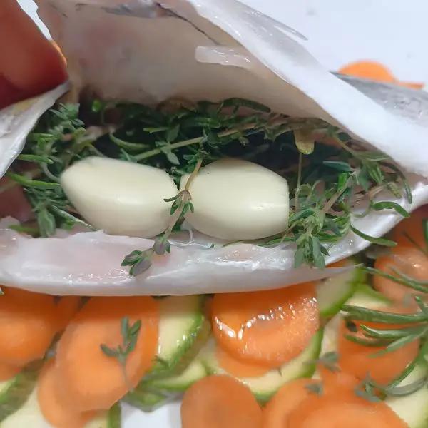 Immagine dello step: Sbucciare l'aglio,tagliarlo in due e infarlo nella pancia del pesce insieme al rosmarino e il timo.Salare leggermente.