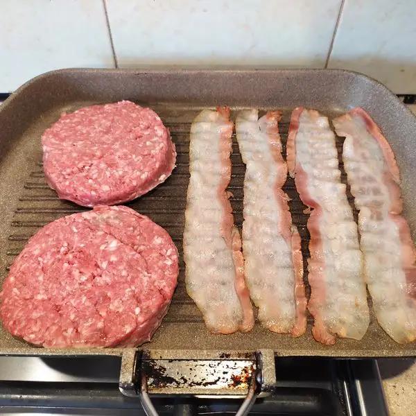 Immagine dello step: Per prima cosa cuocere gli hamburger ed il bacon in una piastra calda. Aggiungere sale e pepe a piacere.