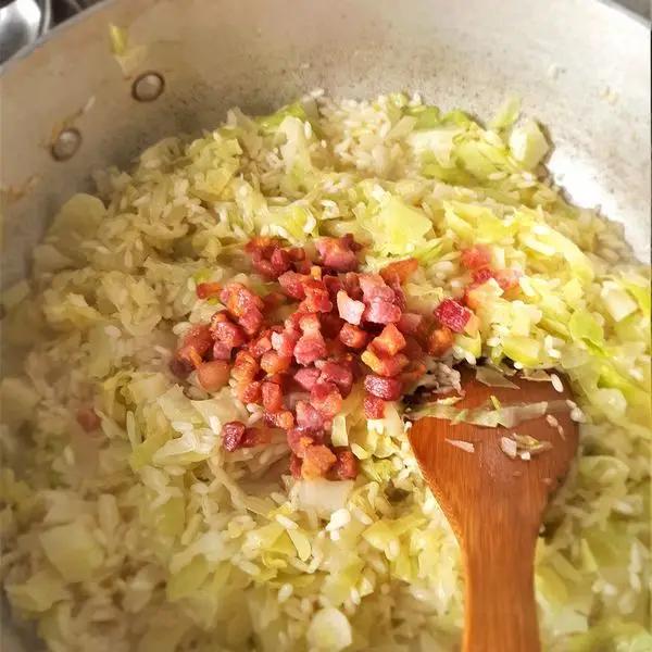 Immagine dello step: Continuate a cuocere il riso, aggiungendo poco alla volta il brodo per 13 minuti. Ora unite anche i dadini rosolati di pancetta affumicata e completate la cottura per altri 5 minuti.