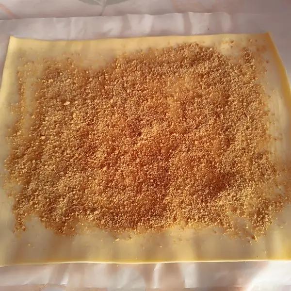 Immagine dello step: Stendere il rotolo di pasta sfoglia, spennellare con la noce di burro,e cospargere dei biscotti triturati