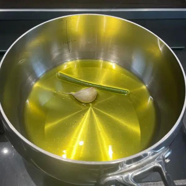 Immagine dello step: In una casseruola in acciaio mettere abbondante olio con aglio in camicia e il gambo del prezzemolo